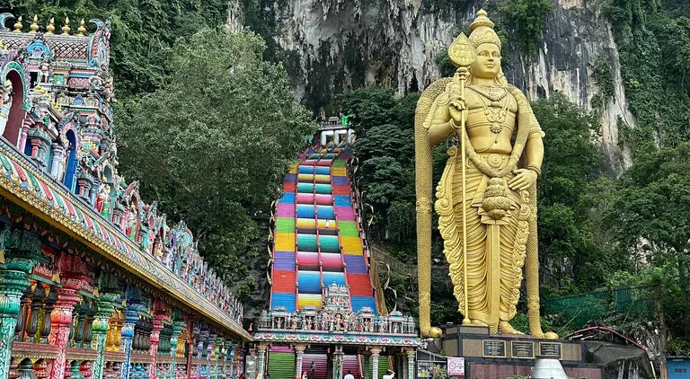 Gold statue of a deity with colorful steps and temple in the background in Kuala Lumpur