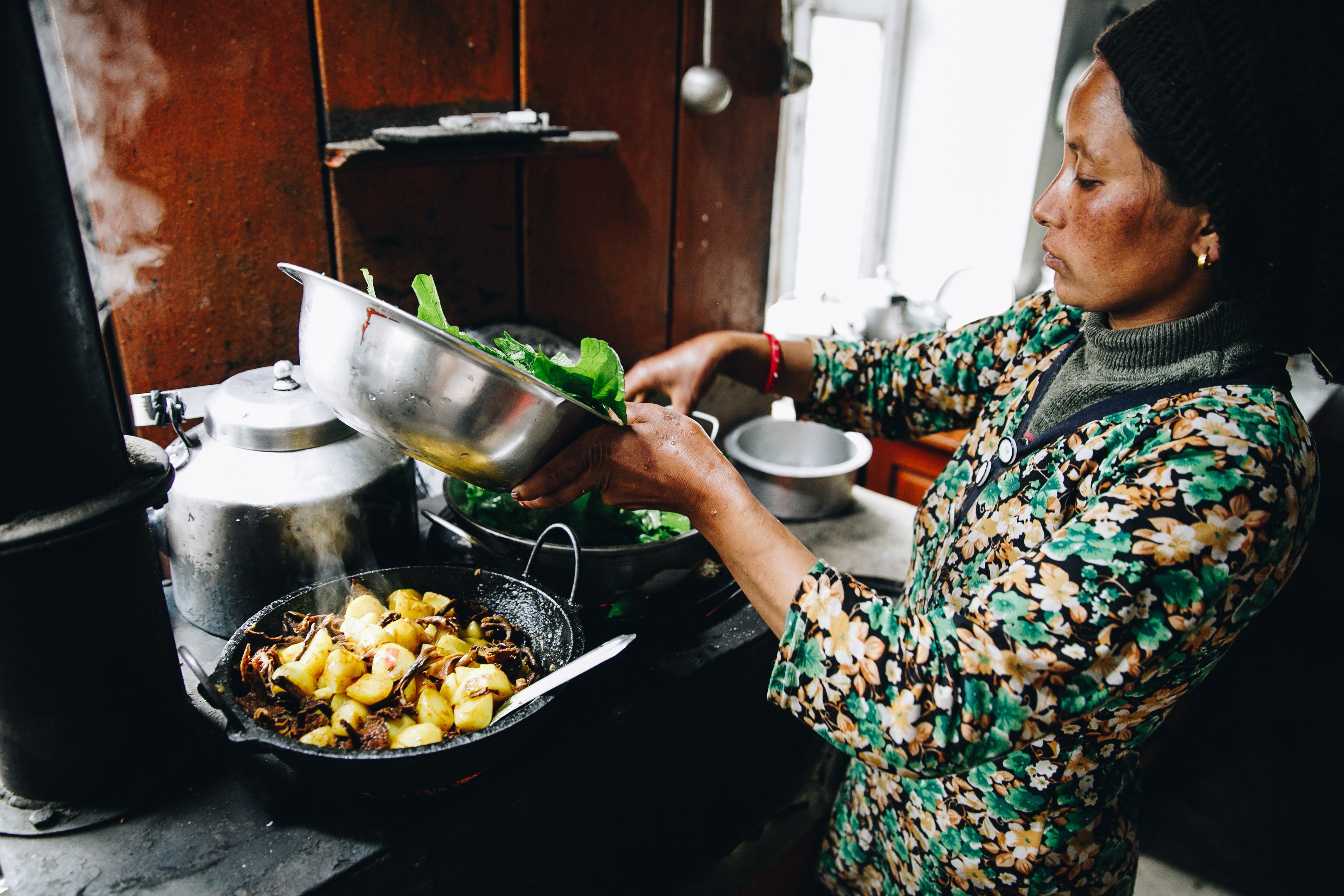 Woman cooking in a kitchen, adding greens to a pan. Cultural Immersive Adventure Programs available