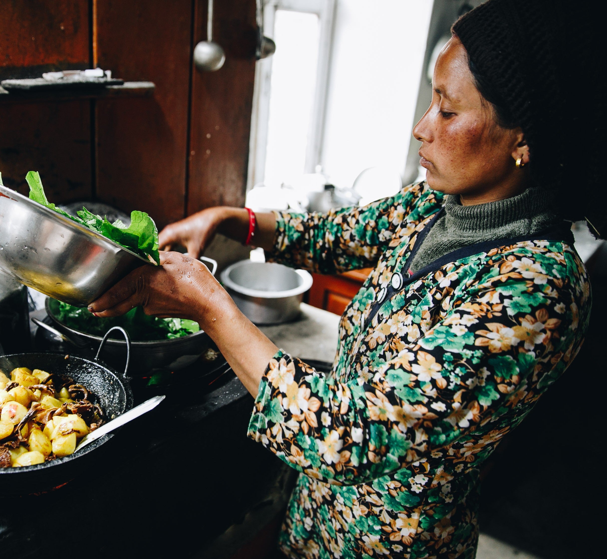 Woman cooking in a kitchen, adding greens to a pan. Cultural Immersive Adventure Programs