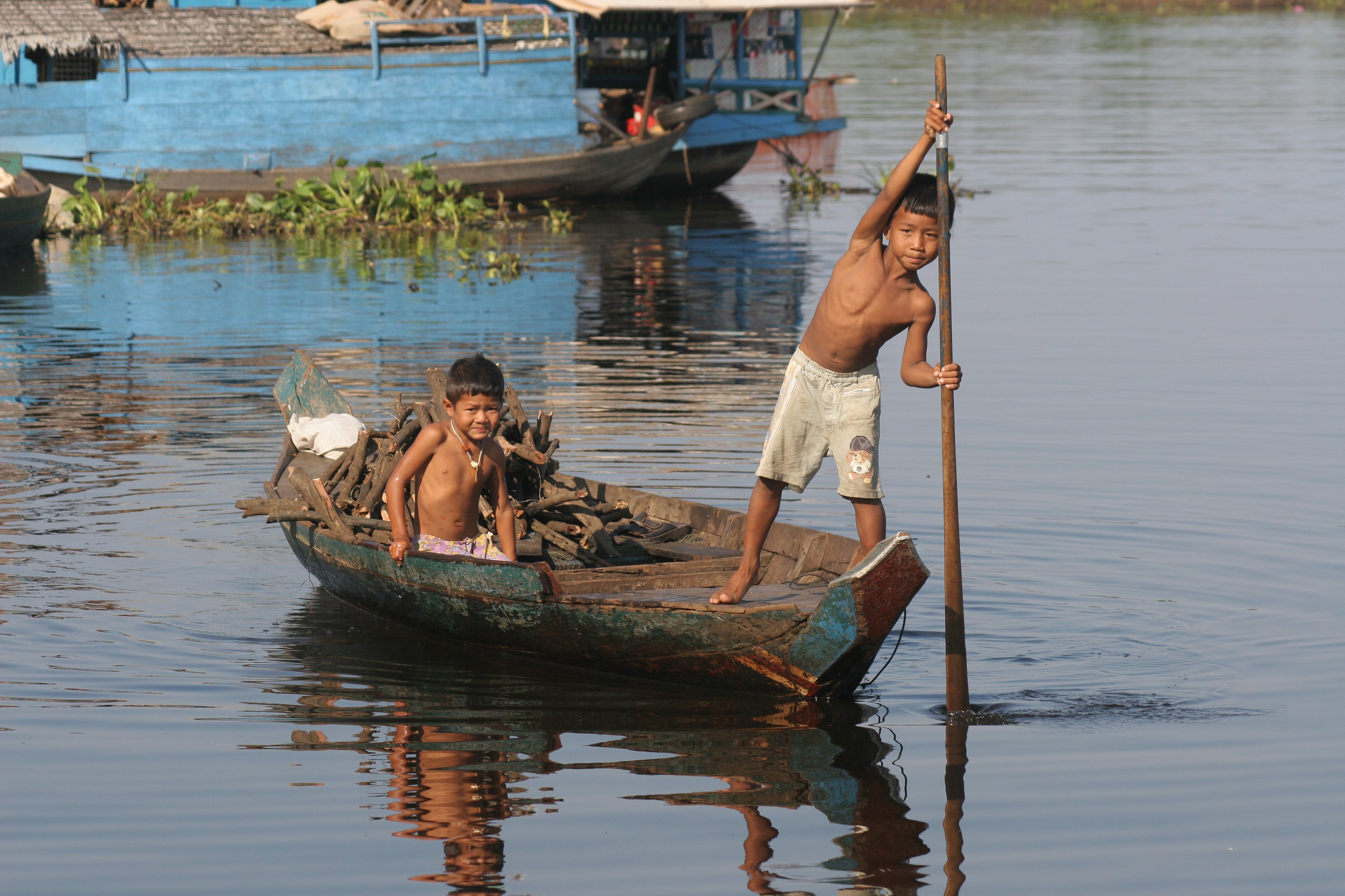 Two children in a small boat on a calm body of water with another boat in the background in Malaysia